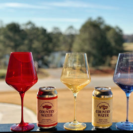 A railing with cans of Country Water and colorful wine glasses in front of a country scene